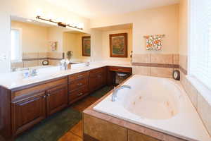 Full bathroom featuring a jetted tub, double vanity, and dark tile patterned floors