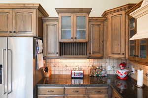 Kitchen with glass insert cabinets, high quality fridge, and dark stone countertops