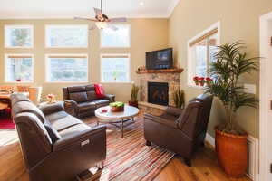 Living area with a stone fireplace, crown molding, light wood-type flooring, and ceiling fan