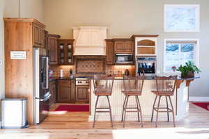 Kitchen featuring a kitchen breakfast bar, an island with sink, stainless steel appliances, and premium range hood