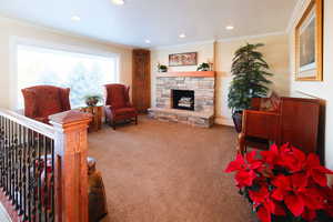 Living area with a stone fireplace, carpet floors, crown molding, and recessed lighting