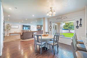 Dining area featuring a textured ceiling, dark wood-style flooring, a fireplace, a chandelier, and recessed lighting