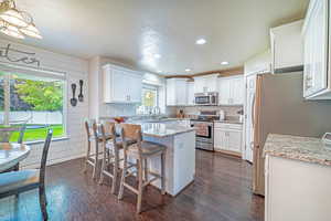 Kitchen featuring appliances with stainless steel finishes, light stone countertops, white cabinets, a textured ceiling, and a breakfast bar