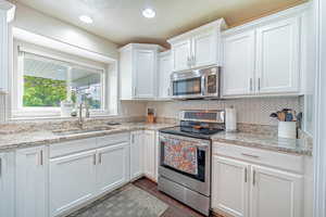 Kitchen with appliances with stainless steel finishes, white cabinets, decorative backsplash, light stone countertops, and recessed lighting