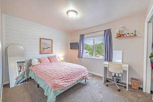Bedroom featuring wooden walls, a textured ceiling, carpet, an accent wall, and an office area