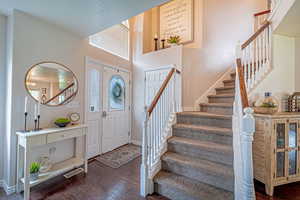 Entryway with stairs, dark wood-style flooring, and a towering ceiling
