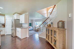 Kitchen with a textured ceiling, white cabinets, backsplash, freestanding refrigerator, and light stone counters