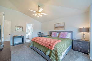 Carpeted bedroom featuring vaulted ceiling, connected bathroom, and a ceiling fan