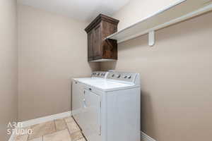 Laundry room with travertine flooring, cabinet space, and washer and clothes dryer.