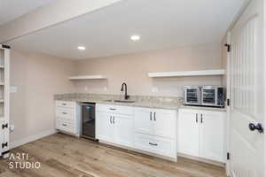 Kitchen featuring open shelves, white cabinetry, LVP flooring, small refrigerator, and granite countertops.  Microwave is located under the counter top.