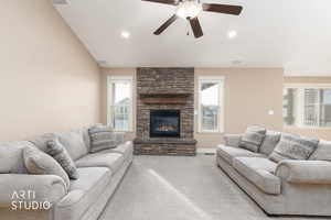 Carpeted living room with a stone gas fireplace, vaulted ceiling, and ceiling fan