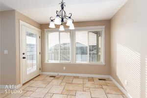 Unfurnished dining area with travertine flooring, a chandelier, and healthy amount of natural light.  Door exits to south facing covered deck.