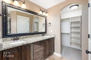 Primary bathroom with double vanity, travertine floor, a spacious closet, and closet with light carpet