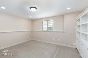Bedroom 5 or office with light carpet, recessed lighting and tasteful freestanding wall unit.