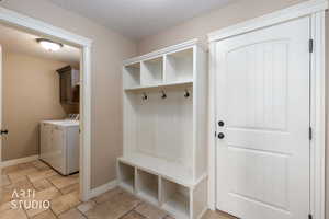 Mudroom featuring a textured ceiling, washer and dryer, and travertine flooring.  Door exits to garage.