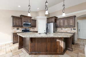 Kitchen featuring dark brown cabinetry, decorative backsplash, vaulted ceiling, and pendant lighting.