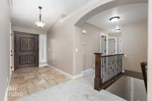 Foyer featuring arched walkways, light carpet, travertine floors, and vaulted ceiling.