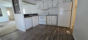 Kitchen with white appliances, dark countertops, white cabinetry, and under cabinet range hood