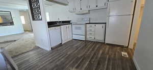 Kitchen featuring white appliances, white cabinets, dark countertops, under cabinet range hood, and dark wood finished floors