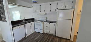 Kitchen featuring white appliances, white cabinetry, dark countertops, and dark wood finished floors
