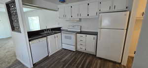 Kitchen featuring white appliances, white cabinets, dark countertops, dark wood finished floors, and under cabinet range hood