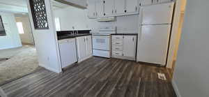Kitchen featuring white appliances, dark countertops, white cabinets, under cabinet range hood, and dark wood-style floors