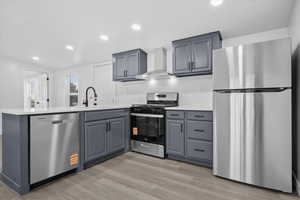 Kitchen featuring stainless steel appliances, a peninsula, wall chimney range hood, recessed lighting, and light wood-style flooring