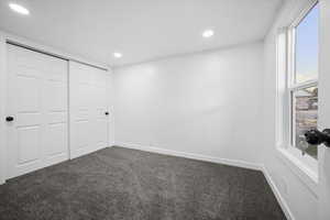 Unfurnished bedroom featuring dark carpet, recessed lighting, and a closet