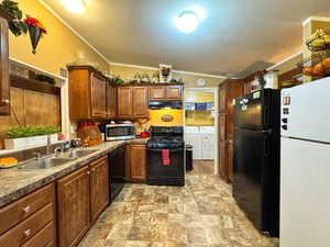 Kitchen featuring black appliances, washing machine and dryer, crown molding, stone finish floors, and lofted ceiling