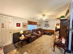 Carpeted living room featuring ornamental molding, vaulted ceiling, a ceiling fan, a wainscoted wall, and wood walls
