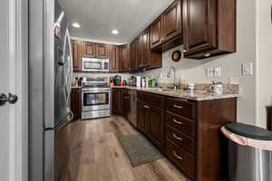 Kitchen featuring stainless steel appliances, dark brown cabinets, light stone countertops, light wood-style floors, and recessed lighting