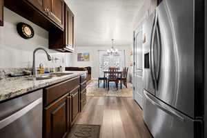 Kitchen with appliances with stainless steel finishes, dark brown cabinets, a chandelier, light stone counters, and dark wood finished floors