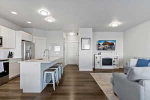 Kitchen featuring a breakfast bar, appliances with stainless steel finishes, a fireplace, an island with sink, and white cabinets