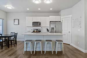Kitchen with white cabinetry, appliances with stainless steel finishes, a center island with sink, a breakfast bar area, and tasteful backsplash