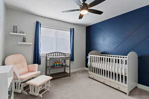 Bedroom with a crib, light colored carpet, a ceiling fan, and a textured ceiling