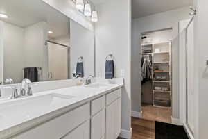 Full bath featuring a stall shower, double vanity, dark wood-style floors, and a walk in closet