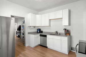 Kitchen featuring appliances with stainless steel finishes, white cabinetry, light wood-style flooring, and a textured ceiling