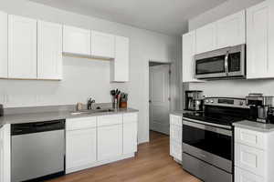 Kitchen with appliances with stainless steel finishes, white cabinets, and light wood finished floors