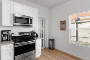 Kitchen with stainless steel appliances, white cabinets, and light wood-type flooring
