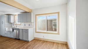 Kitchen with gray cabinets, tasteful backsplash, dishwasher, light wood finished floors, and beamed ceiling
