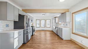 Kitchen with gray cabinetry, tasteful backsplash, light wood-type flooring, stainless steel appliances, and beam ceiling