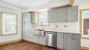 Kitchen with gray cabinetry, dishwasher, light stone countertops, light wood-style flooring, and backsplash