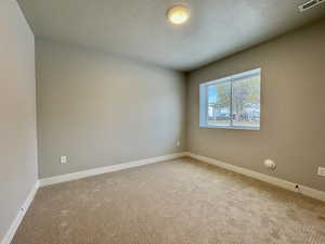 Carpeted spare room with a textured ceiling and baseboards