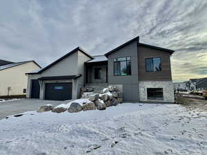 View of front of house with stone siding, an attached garage, and driveway