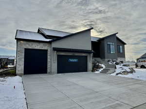 Snow covered property featuring stone siding, an attached garage, concrete driveway, a metal roof, and a standing seam roof