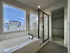 Bathroom with dark tile patterned flooring, a spacious closet, a shower stall, a garden tub, and recessed lighting