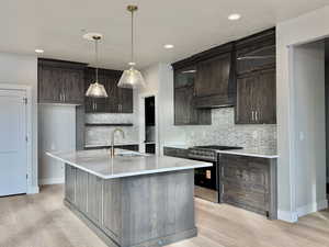 Kitchen with tasteful backsplash, stainless steel range with gas cooktop, dark brown cabinetry, light stone countertops, and recessed lighting