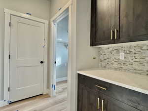 Bar area with dark brown cabinetry, light stone counters, backsplash, and light wood-style flooring