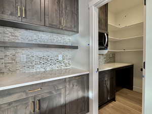 Bar with dark brown cabinetry, tasteful backsplash, light wood-style flooring, light stone countertops, and open shelves