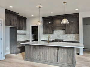 Kitchen with tasteful backsplash, dark brown cabinetry, pendant lighting, light stone countertops, and recessed lighting